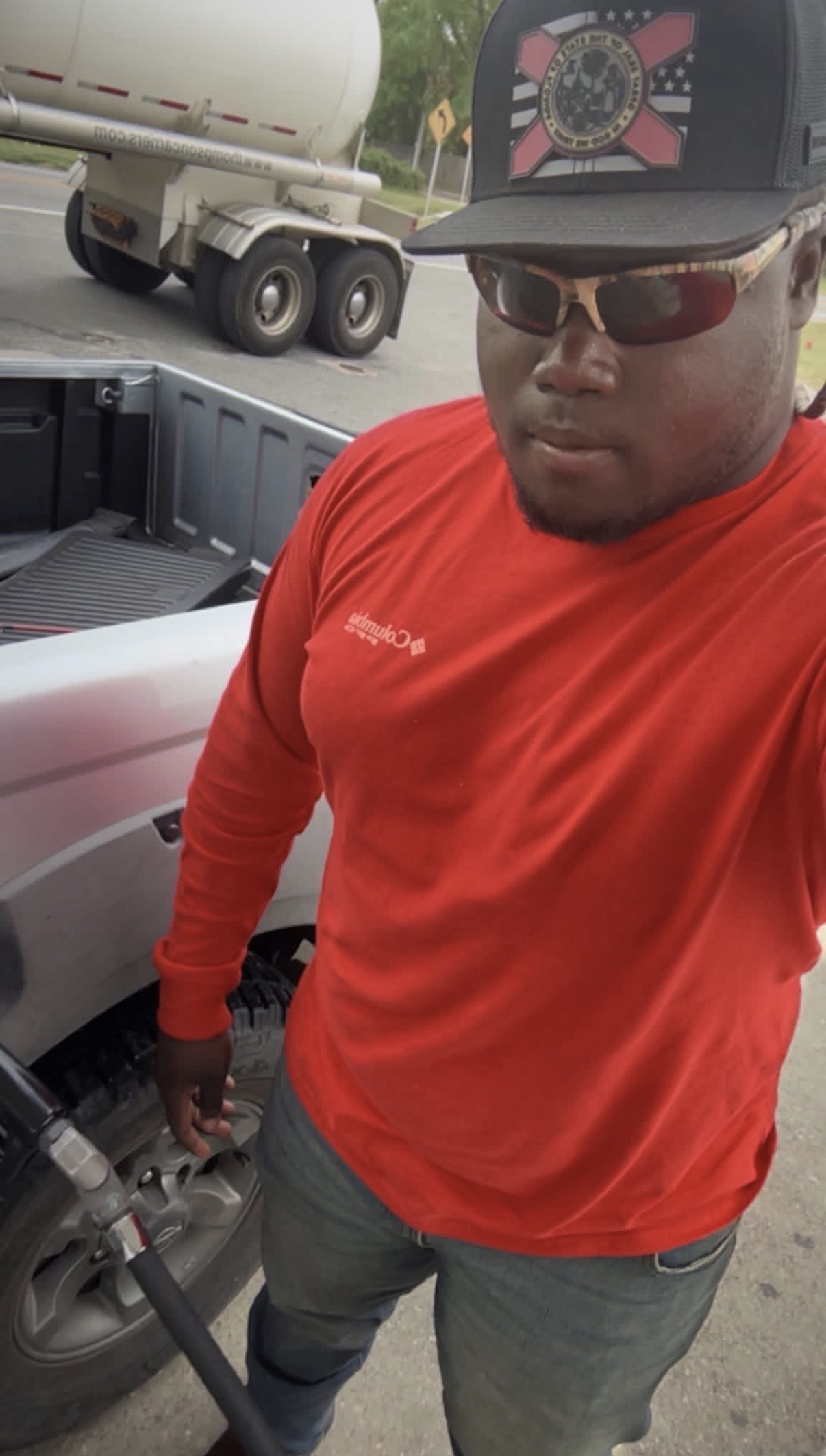 Mahri in a red long-sleeve shirt, cap and sunglasses standing beside a truck during his second job.